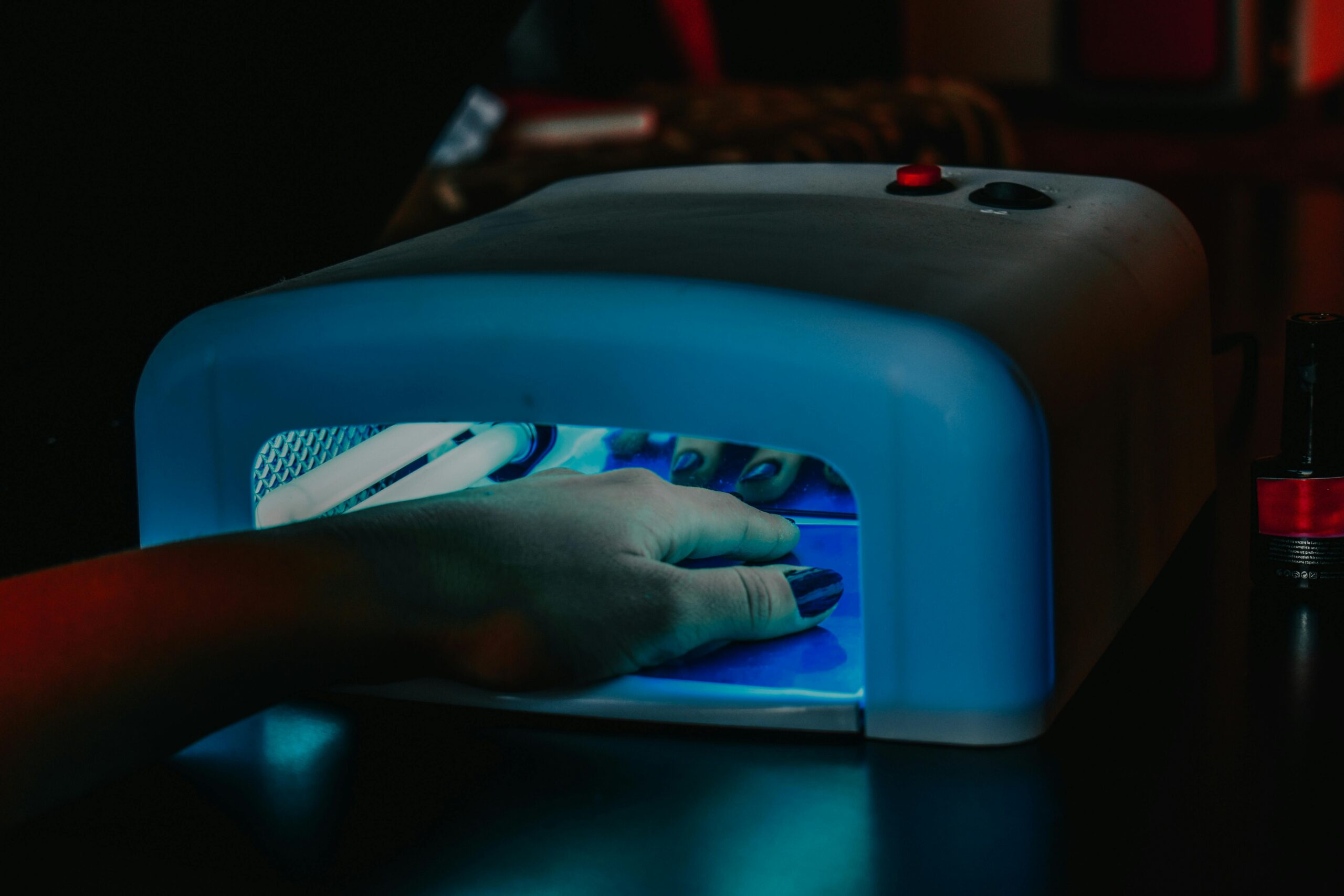pexels photo 9099607 9099607 A hand with manicured nails being cured under a blue LED lamp for gel polish.